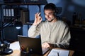 Young handsome man working using computer laptop at night smiling positive doing ok sign with hand and fingers Royalty Free Stock Photo