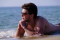 A young handsome man of 25-30 years old, a brunette, in weed sunglasses, lies relaxed on the sand on the beach of the sea coast Royalty Free Stock Photo