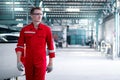 Young handsome mechanic man in red uniform walking through row of vehicle at car service, auto mechanic technician checking, Royalty Free Stock Photo