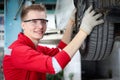 Young handsome mechanic in red uniform working with lifted vehicle, auto mechanic checking wheel at garage, technician check, Royalty Free Stock Photo