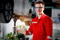 Young handsome mechanic in red uniform working with lifted vehicle, auto mechanic checking wheel at garage, technician check, Royalty Free Stock Photo