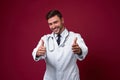 Young handsome modern doctor in a white medical gown stands in the studio on a red background. Student trainee of a medical Royalty Free Stock Photo