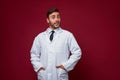 Young handsome modern doctor in a white medical gown stands in the studio on a red background. Student trainee of a medical Royalty Free Stock Photo
