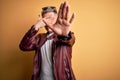 Young handsome modern man wearing fashion leather jacket and sunglasses over yellow background covering eyes with hands and doing Royalty Free Stock Photo