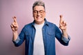 Young handsome modern man wearing glasses and denim jacket over pink isolated background gesturing finger crossed smiling with Royalty Free Stock Photo