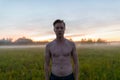 Young handsome muscular man shirtless against grass field with fog in the break of dawn