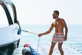 Young handsome muslim captain wearing shorts pulling a rope of a yacht or boat in order to control it standing on berth