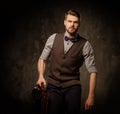 Young handsome old-fashioned man with briefcase posing on dark background. Royalty Free Stock Photo