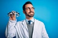 Young handsome optical man with beard holding optometry glasses over blue background smiling looking to the side and staring away Royalty Free Stock Photo