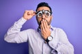 Young handsome optical man with beard wearing optometry glasses over purple background cover mouth with hand shocked with shame