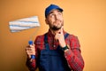 Young handsome painter man painting wall using roller over isolated yellow background serious face thinking about question, very Royalty Free Stock Photo