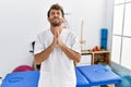 Young handsome physiotherapist man working at pain recovery clinic begging and praying with hands together with hope expression on Royalty Free Stock Photo