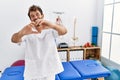 Young handsome physiotherapist man working at pain recovery clinic smiling in love doing heart symbol shape with hands Royalty Free Stock Photo