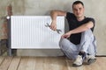 Young handsome plumber sitting on floor with wrench in hand near