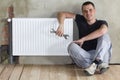 Young handsome plumber sitting on floor with wrench in hand near