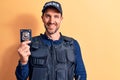 Young handsome policeman wearing uniform and bulletprof holding police badge looking positive and happy standing and smiling with Royalty Free Stock Photo
