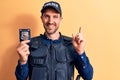 Young handsome policeman wearing uniform and bulletprof holding police badge smiling happy pointing with hand and finger to the Royalty Free Stock Photo