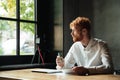 Young handsome readhead bearded man sitting on the workplace at