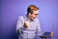 Young handsome redhead businessman working using laptop over purple background screaming proud and celebrating victory and success Royalty Free Stock Photo