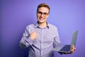 Young handsome redhead businessman working using laptop over purple background with surprise face pointing finger to himself Royalty Free Stock Photo