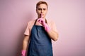 Young handsome redhead cleaner man doing housework wearing apron and gloves asking to be quiet with finger on lips Royalty Free Stock Photo