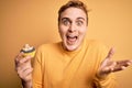 Young handsome redhead man eating sweet chocolate cupcake dessert over yellow background celebrating victory with happy smile and Royalty Free Stock Photo