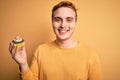 Young handsome redhead man eating sweet chocolate cupcake dessert over yellow background looking positive and happy standing and Royalty Free Stock Photo