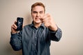 Young handsome redhead man holding broken smartphone showing cracked screen annoyed and frustrated shouting with anger, yelling