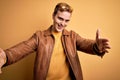 Young handsome redhead man wearing casual leather jacket over isolated yellow background looking at the camera smiling with open Royalty Free Stock Photo