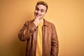 Young handsome redhead man wearing casual leather jacket over isolated yellow background looking confident at the camera smiling Royalty Free Stock Photo