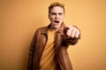 Young handsome redhead man wearing casual leather jacket over isolated yellow background pointing displeased and frustrated to the Royalty Free Stock Photo