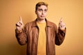 Young handsome redhead man wearing casual leather jacket over isolated yellow background Pointing up looking sad and upset, Royalty Free Stock Photo