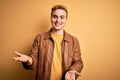 Young handsome redhead man wearing casual leather jacket over isolated yellow background smiling cheerful with open arms as Royalty Free Stock Photo