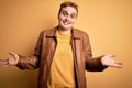 Young handsome redhead man wearing casual leather jacket over isolated yellow background smiling showing both hands open palms, Royalty Free Stock Photo