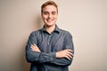 Young handsome redhead man wearing casual shirt standing over isolated white background happy face smiling with crossed arms Royalty Free Stock Photo