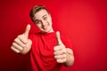 Young handsome redhead man wearing casual t-shirt over isolated red background approving doing positive gesture with hand, thumbs Royalty Free Stock Photo