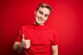 Young handsome redhead man wearing casual t-shirt over isolated red background doing happy thumbs up gesture with hand Royalty Free Stock Photo