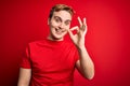 Young handsome redhead man wearing casual t-shirt over isolated red background smiling positive doing ok sign with hand and Royalty Free Stock Photo