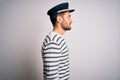 Young handsome sailor man with beard wearing navy striped uniform and captain hat looking to side, relax profile pose with natural Royalty Free Stock Photo