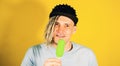 Young handsome satisfied man with dreadlocks in black cap eating ice cream on yellow background. Joyful guy in blue t Royalty Free Stock Photo