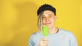 Young handsome satisfied man with dreadlocks in black cap eating ice cream on yellow background. Joyful guy in blue t Royalty Free Stock Photo