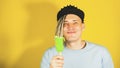 Young handsome satisfied man with dreadlocks in black cap eating ice cream on yellow background. Joyful guy in blue t Royalty Free Stock Photo