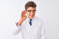 Young handsome sciencist man wearing glasses and coat over isolated white background smiling with hand over ear listening an Royalty Free Stock Photo