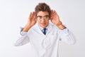 Young handsome sciencist man wearing glasses and coat over isolated white background Trying to hear both hands on ear gesture, Royalty Free Stock Photo