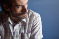 A young handsome serious bearded man with striped shirt sitting and looking away against light blue background. Thinking about the Royalty Free Stock Photo