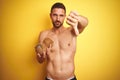 Young handsome shirtless man holding exotic tropical coconut over isolated yellow background with angry face, negative sign Royalty Free Stock Photo