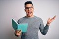 Young handsome smart student man reading book over isolated white background very happy and excited, winner expression celebrating Royalty Free Stock Photo