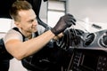 Young handsome smiling Caucasian man in black protective gloves using cleaning brush and removing dust from car control Royalty Free Stock Photo