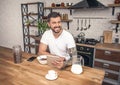 Young handsome smiling man is having his breakfast cereals with milk at the kitchen and reading morning news on the tablet Royalty Free Stock Photo