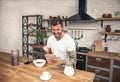 Young handsome smiling man is having his breakfast cereals with milk at the kitchen and reading morning news on the tablet been Royalty Free Stock Photo